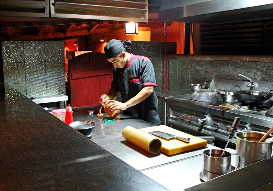 En kock arbetar vid en arbetsbänk i rostfritt stål i ett restaurangkök med professionell utrustning.